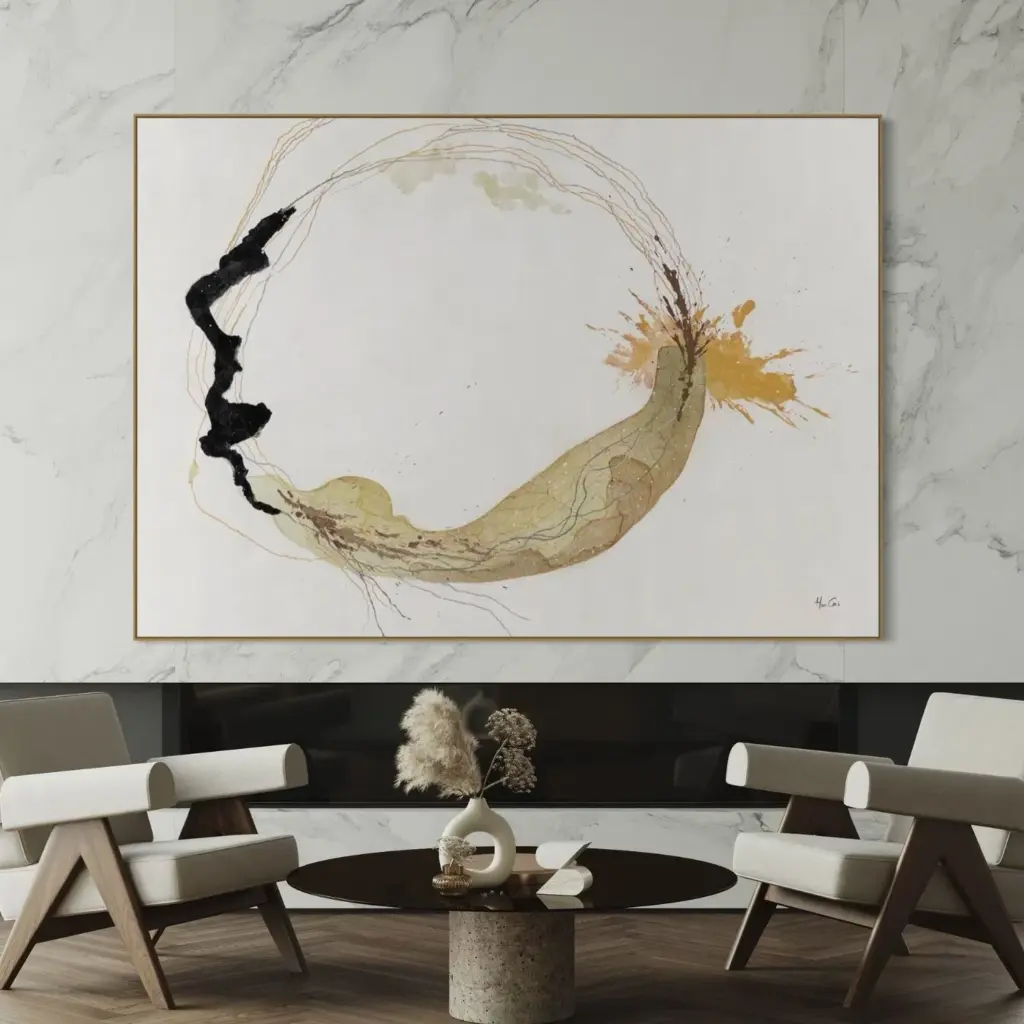 A framed abstract painting featuring a large black circular brushstroke and gold accents, hanging in a living area above two armchairs and a coffee table.
